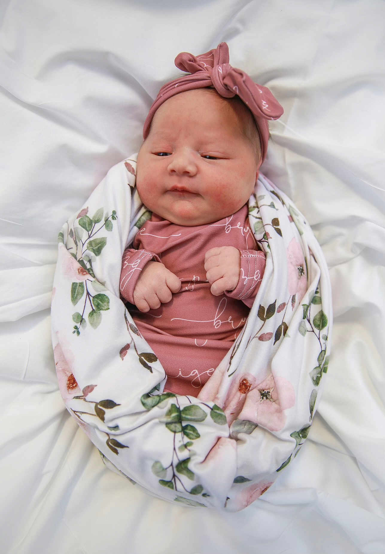 Brynley is registered to the contest to win money with this photo: newborn, baby, swaddled, blanket, headband, onesie, sleepy, infant, cute, portrait, soft, floral, white_background, hands, clothing, wrapped, peaceful, indoors, closeup, child