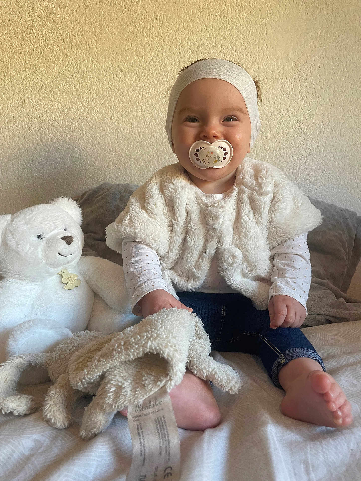 Djulia participe au concours pour gagner de l'argent avec cette photo : baby, child, pacifier, headband, fluffy_clothing, blanket, teddy_bear, bed, smile, happy, indoor, soft_toys, foot, jeans, long_sleeve_shirt, cushion, wall, person, infant, cute