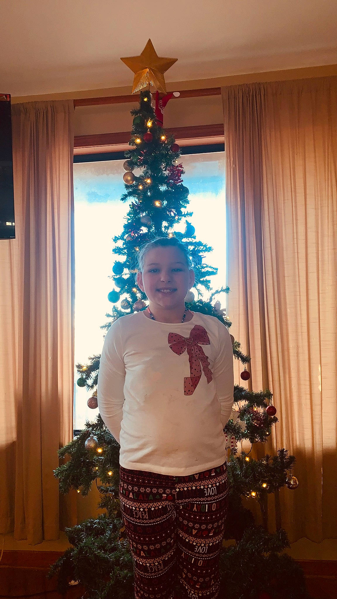 Bayleigh is registered to the contest to win money with this photo: christmas, christmas_decoration, christmas_eve, christmas_ornament, christmas_tree, curtain, decoration, event, holiday, holiday_ornament, interior_design, joy, light, ornament, person, plant, standing, trunk, white, window