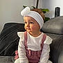 baby, bow, child, couch, cushion, cute, face, fashion, hands, headband, indoor, infant, long_sleeve, looking_away, pink_overalls, plant, portrait, ruffles, seated, white_top