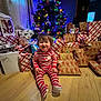 toddler, child, christmas_tree, presents, gift_wrapping, holiday, indoors, floor, smile, festive_lights, wooden_floor, red_stripes, pajamas, happy, holiday_decor, wrapped_gifts, celebration, festive, home, cute