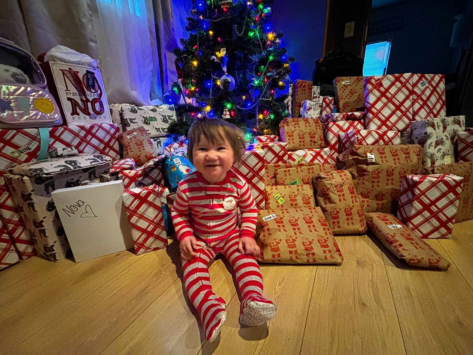 Novs joined the competition — help win amazing prizes! toddler, child, christmas_tree, presents, gift_wrapping, holiday, indoors, floor, smile, festive_lights, wooden_floor, red_stripes, pajamas, happy, holiday_decor, wrapped_gifts, celebration, festive, home, cute