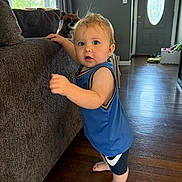 Zane joined the competition — help win amazing prizes! toddler, child, dog, indoor, couch, wooden_floor, blue_clothing, barefoot, standing, curious, pet, living_room, window, door, natural_light, furniture, home, person, face, smiling