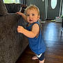 toddler, child, dog, indoor, couch, wooden_floor, blue_clothing, barefoot, standing, curious, pet, living_room, window, door, natural_light, furniture, home, person, face, smiling