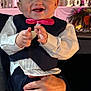Zane is registered to the contest to win money with this photo: baby, child, smile, formal_wear, bow_tie, vest, pants, hand, adult_hand, indoor, celebration, decor, flowers, lighting, portrait, happy, cute, person, event, background