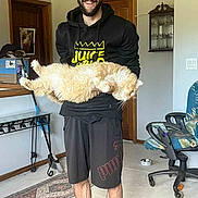 Fluffy joined the competition — help win amazing prizes! man, cat, indoor, glasses, hoodie, shorts, rug, chair, floor, door, cabinet, smiling, beard, orange_cat, holding, pet, casual, home, furniture, happy