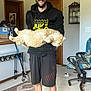 man, cat, indoor, glasses, hoodie, shorts, rug, chair, floor, door, cabinet, smiling, beard, orange_cat, holding, pet, casual, home, furniture, happy