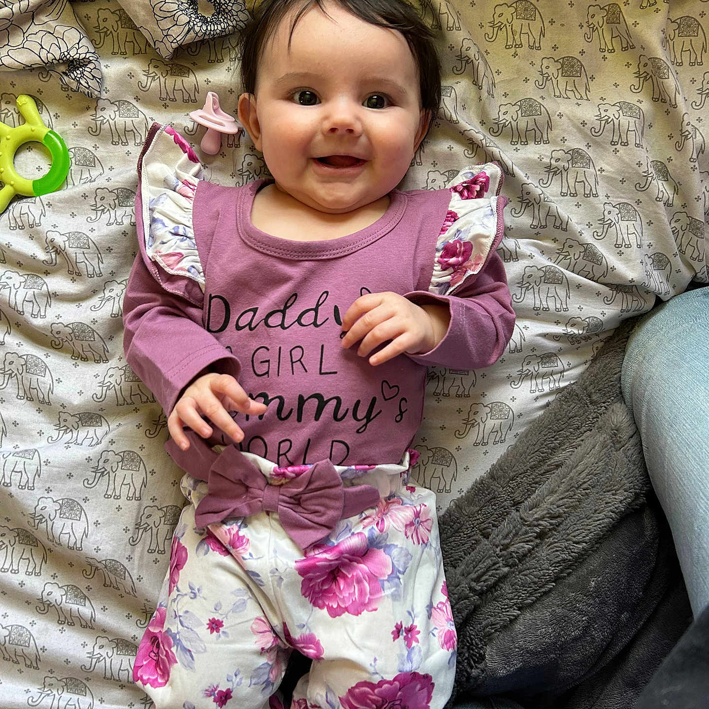 Brynleigh is registered to the contest to win money with this photo: baby, bed, blanket, child, clothing, cute, elephant_pattern, floral_pants, girl, happy, indoor, infant, lying_down, pacifier, person, portrait, purple_top, smiling, soft_texture, toy
