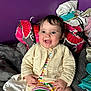 Brynleigh is registered to the contest to win money with this photo: baby, bag, bed, blanket, child, colorful, cozy, cute, happy, indoors, infant, knitted_cardigan, person, portrait, purple_wall, sitting, smiling, soft_texture, striped_clothing, warm
