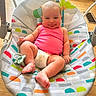 Ella is registered to the contest to win money with this photo: baby, infant, smiling, pink_tank_top, diaper, baby_seat, colorful_pattern, tongue_out, indoor, wooden_floor, pacifier, cheerful, cute, child, person, plush, playful, happy, home, portrait