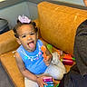 toddler, child, toy, couch, indoor, playful, blue_shirt, person, smile, tongue_out, hair_bow, earrings, plastic_toys, casual, home, carpet, trash_can, happy, family, fun