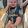 Jose is registered to the contest to win money with this photo: baby, high_chair, blue_onesie, smiling, tongue_out, happy, infant, sitting, wooden_floor, indoor, straps, safety_harness, cute, child, person, face, raised_arm, playful, home, bright