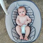 Jose is registered to the contest to win money with this photo: baby, infant, blue_eyes, diaper, baby_seat, cushion, concrete_floor, barefoot, looking_up, cute, child, small_hands, small_feet, indoor, seat_belt, striped_cushion, plush, person, portrait, young_child