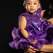 Skyler joined the competition — help win amazing prizes! toddler, child, purple_dress, sparkles, ruffles, hair_bows, curly_hair, silver_shoes, portrait, studio_lighting, black_background, cute, person, holding, fashion, elegant, baby, face, expression, hands