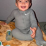 Jordan joined the competition — help win amazing prizes! baby, smiling, gray_onesie, blanket, toy, bottle, indoor, child, happy, face, infant, sitting, cute, person, young_child, home, playtime, cozy, baby_toys, cheerful