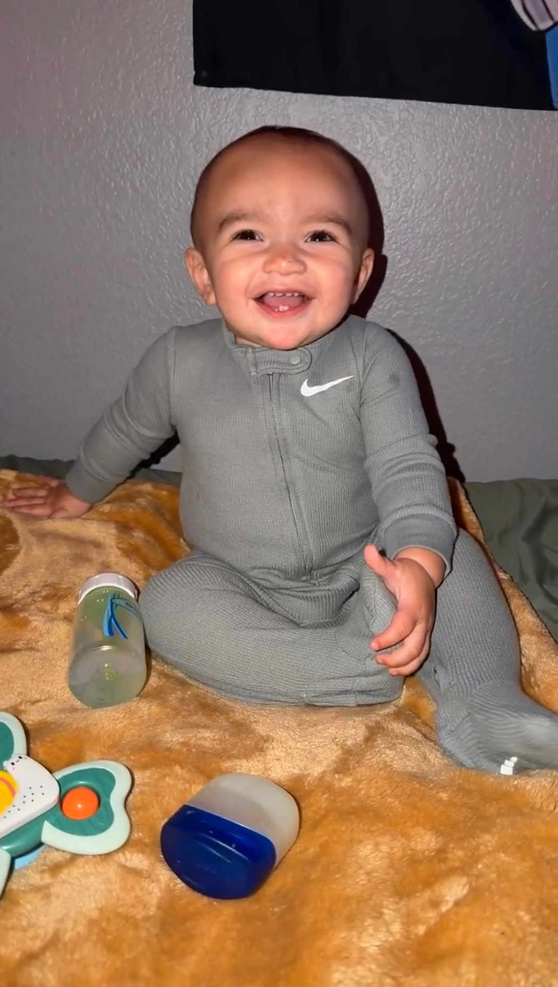 Jordan joined the competition — help win amazing prizes! baby, smiling, gray_onesie, blanket, toy, bottle, indoor, child, happy, face, infant, sitting, cute, person, young_child, home, playtime, cozy, baby_toys, cheerful