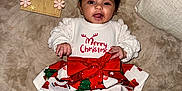 Azayla joined the competition — help win amazing prizes! baby, blanket, celebration, child, christmas_outfit, clothing, couch, cute, festive, happy, holiday, indoors, infant, months_marker, portrait, red_bow, sitting, smiling, white_socks, wooden_sign