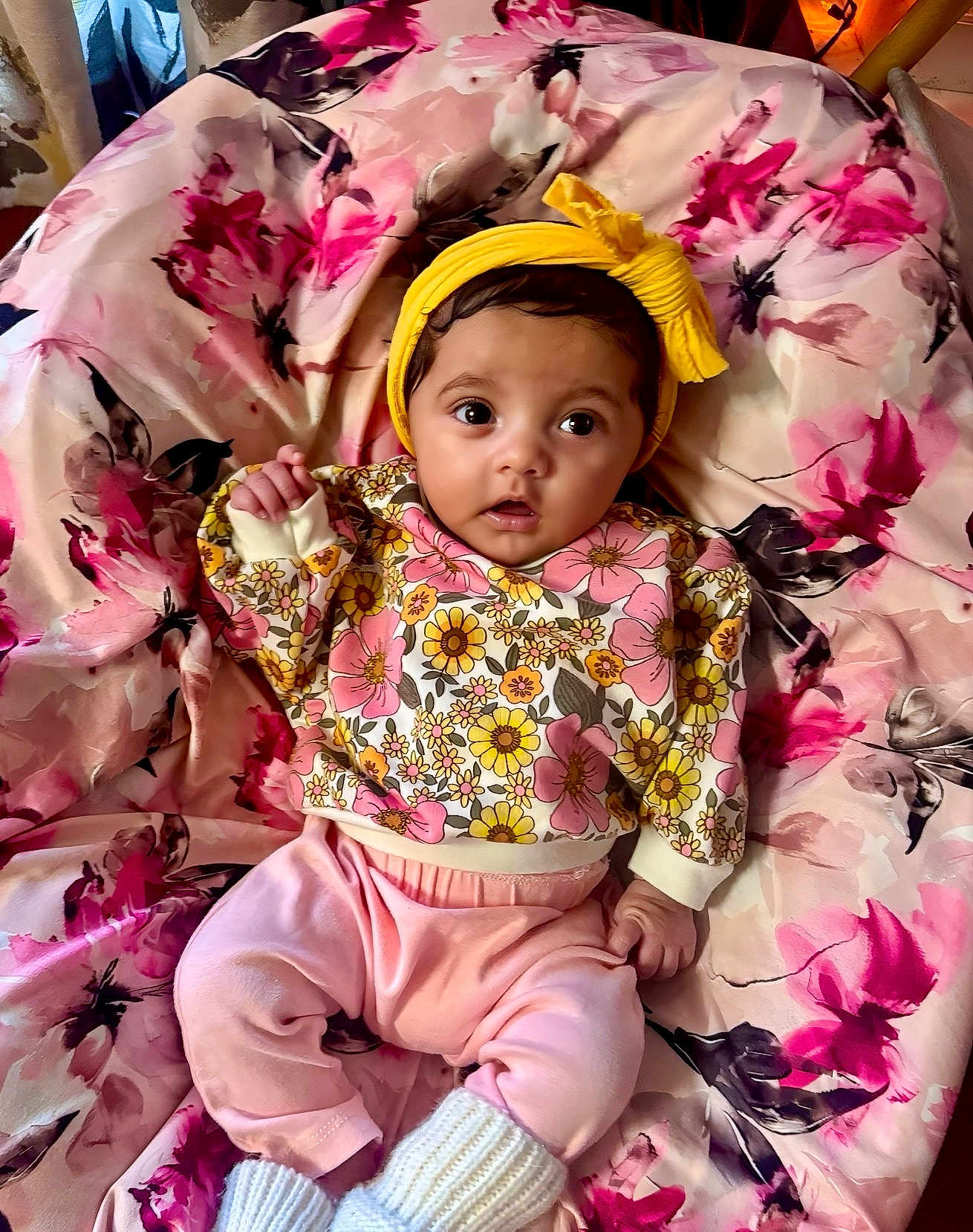 Azayla is registered to the contest to win money with this photo: adorable, baby, blanket, child, clothing, colorful, cute, expression, face, floral_pattern, indoors, infant, knitted_booties, lying_down, pink_pants, portrait, small_hand, soft_toys, yellow_headband, young
