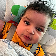 Royal is registered to the contest to win money with this photo: baby, child, curly_hair, blanket, yellow_clothing, face, eyes, infant, close_up, indoor, baby_seat, harness, cute, expression, portrait, soft_texture, comfort, young_child, looking_at_camera, toddler
