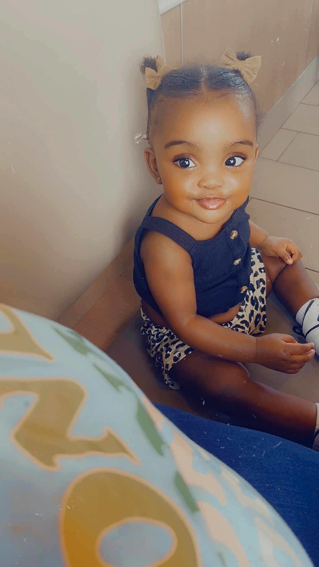 Aaliyah is registered to the contest to win money with this photo: toddler, child, smiling, sitting, indoor, pigtails, hair_bows, black_top, leopard_print, shorts, socks, shoes, floor, tile_floor, cute, portrait, happy, young_child, baby, person
