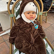 Youssef Chawachi participe au concours pour gagner de l'argent avec cette photo : baby, child, infant, bear_suit, knitted_hat, pacifier, chair, woven_chair, outdoor, pavement, brown_clothing, cute, expression, winter_clothing, seated, person, face, cold_weather, wearing, costume