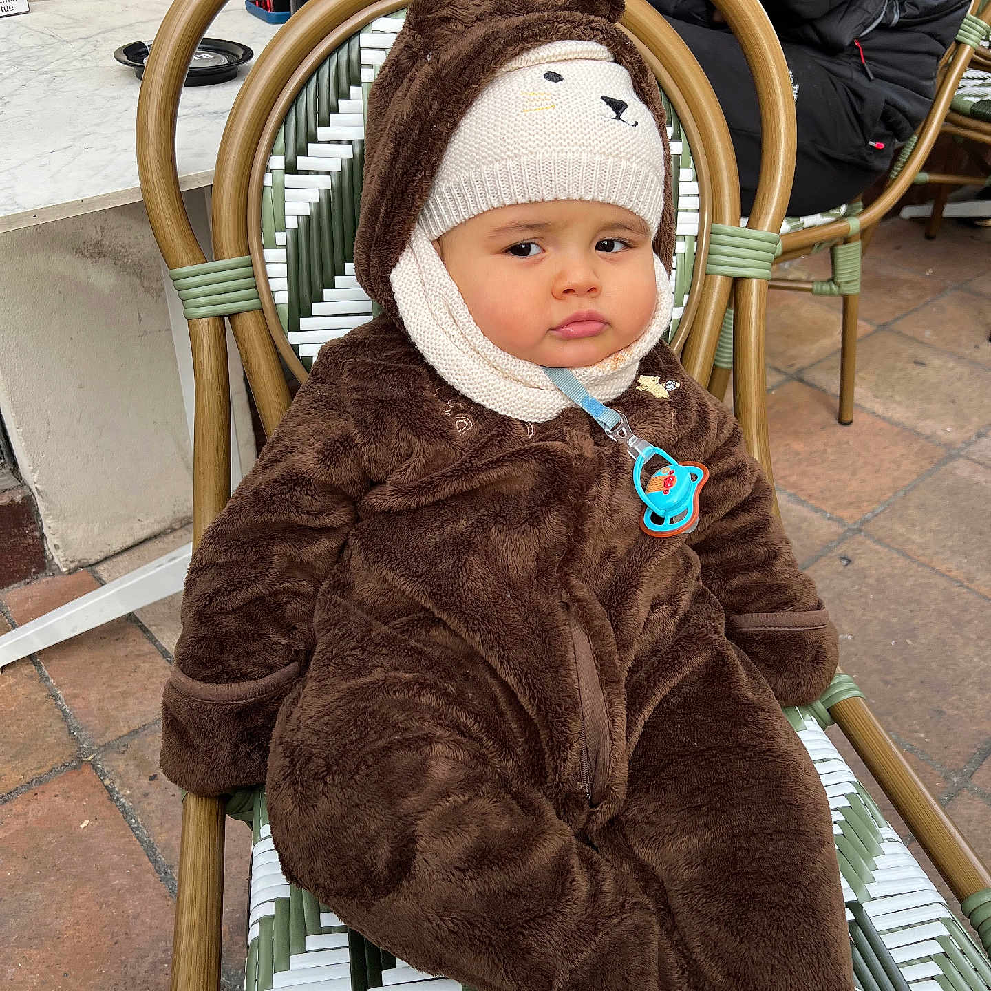Youssef Chawachi participe au concours pour gagner de l'argent avec cette photo : baby, bear_suit, brown_clothing, chair, child, cold_weather, costume, cute, expression, face, infant, knitted_hat, outdoor, pacifier, pavement, person, seated, wearing, winter_clothing, woven_chair