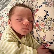 Kristopher is registered to the contest to win money with this photo: baby, sleeping, newborn, face, hand, pillow, floral, pattern, striped_clothing, bed, blanket, rest, peaceful, indoors, closeup, skin, cute, infant, portrait, cozy