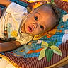 baby, child, infant, curly_hair, play_mat, colorful, animal_pattern, flower_pattern, white_shirt, expression, wide_eyes, cute, indoors, soft_lighting, comfort, portrait, young_child, person, face, lying_down