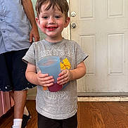 John is registered to the contest to win money with this photo: adult, child, clothing, cup, door, drink, feet, floor, happy, indoor, legs, messy, person, shoes, shorts, smiling, socks, toddler, tshirt, wood