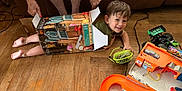 John is registered to the contest to win money with this photo: adult_hands, box, boy, casual, child, couch, cute, floor, fun, green_fan, happy, home, indoor, orange_toy, person, playing, smiling, toy, wooden_floor, young