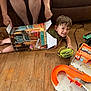 adult_hands, box, boy, casual, child, couch, cute, floor, fun, green_fan, happy, home, indoor, orange_toy, person, playing, smiling, toy, wooden_floor, young