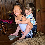 John is registered to the contest to win money with this photo: barefoot, blue_eyes, brown_hair, candid_photo, casual_clothing, children, curly_hair, dog, family, hugging, indoor, large_dog, living_room, pet, piggyback, portrait, siblings, smiling, wood_paneling, wooden_door