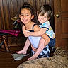 barefoot, blue_eyes, brown_hair, candid_photo, casual_clothing, children, curly_hair, dog, family, hugging, indoor, large_dog, living_room, pet, piggyback, portrait, siblings, smiling, wood_paneling, wooden_door