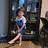 John is registered to the contest to win money with this photo: barefoot, blue_clothing, ceramics, chair, child, display_cabinet, family_photo, furniture, glass_doors, home, indoor, playful_pose, portrait, smiling, standing, teacups, toys, white_shirt, wooden_floor, young_child