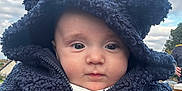 Lorenzo is registered to the contest to win money with this photo: baby, child, hood, jacket, blue, face, outdoor, cloudy_sky, cute, eyes, person, hands, warm_clothing, infant, portrait, winter_wear, headwear, expression, soft_texture, closeup