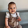 baby, beads, child, clothing, couch, cute, eyes, face, fingers, hand, happy, indoor, infant, overalls, pacifier_clip, portrait, sitting, skin, smile, white_shirt