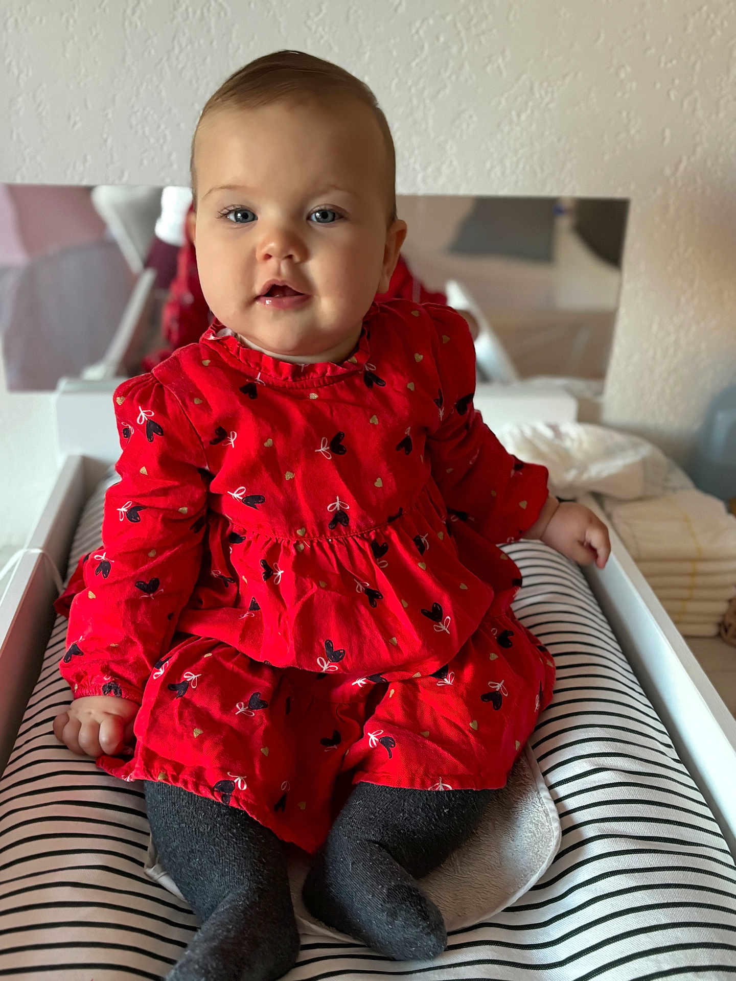 Malya participe au concours pour gagner de l'argent avec cette photo : baby, child, clothing, cozy, curly_hair, cute, face, feet, furniture, heart_pattern, indoors, infant, legs, person, portrait, red_dress, sitting, smiling, soft_lighting, striped_cushion