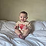 baby, smiling, infant, bed, white_bedding, indoors, child, clothing, happy, portrait, sitting, cute, one_person, wall, room, casual, young_child, feet, hands, head