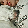 Bobruce is registered to the contest to win money with this photo: person, dog, sleeping_dog, close_up, snuggling, spotted_dog, face, shirt, text_on_shirt, indoor, resting, affection, cute, animal, pet, human, nose, mouth, skin, expression