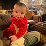 baby, child, red_clothing, smile, indoor, leather_chair, stone_wall, warm_lighting, person, hand, couch, cozy, infant, sitting, portrait, cute, casual, holding, expression, relaxed