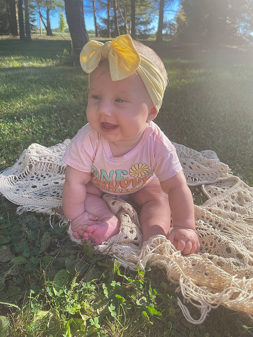 Coraline is registered to the contest to win money with this photo: baby, baby_toddler_clothing, botany, cap, child, fashion_accessory, fun, grass, groundcover, happy, headwear, leaf, light, people_in_nature, person, plant, sitting, smile, soil, sun_hat