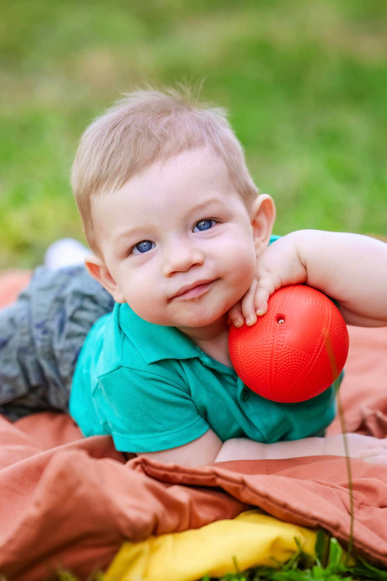 Léo participe au concours pour gagner de l'argent avec cette photo : toddler, child, blue_eyes, outdoor, grass, blanket, orange_ball, green_shirt, shorts, smiling, face, person, baby, relaxed, playful, cute, portrait, summer, daylight, fun