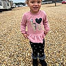 child, girl, smiling, pink_sweater, leggings, boots, headband, outdoor, pebbles, gravel, trailer_park, cloudy_sky, casual_clothing, portrait, standing, happy, cute, fashion, yard, daytime
