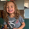 Jadev is registered to the contest to win money with this photo: child, smiling, curly_hair, tshirt, indoor, person, happy, young, face, standing, carpet, television, room, furniture, wood_paneling, casual_clothing, home, bright, portrait, childhood