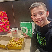 Aleandro a rejoint le concours — aidez-le/la à gagner de superbes lots ! boy, casual, chicken_dips, child, clothing, cup, face, fast_food, food, fries, gift_bag, happy, indoor, packet, person, restaurant, seat, smile, snack, table