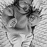 baby, infant, knit_sweater, cozy, blanket, textured_blanket, pacifier_clip, beads, name_beads, cute, tongue_out, lying_down, soft_lighting, black_and_white, portrait, newborn, clothing, hand, face, expression