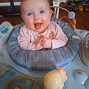 Delilah joined the competition — help win amazing prizes! baby, child, smiling, happy, food, messy_face, baby_seat, toy, indoor, wood_floor, clothing, pink_shirt, face, cute, expression, hands, blue_eyes, infant, play_area, home