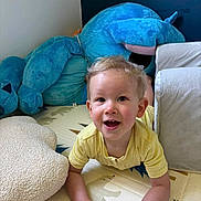 Louis participe au concours pour gagner de l'argent avec cette photo : toddler, child, yellow_shirt, smiling, indoor, play_mat, stuffed_animal, blue_toy, pillow, happy, crawling, face, person, cute, home, soft_toy, childhood, young_child, casual, fun