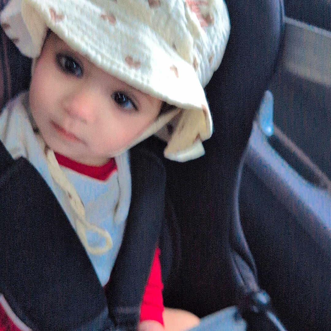 Minha is registered to the contest to win money with this photo: baby, bib, car_interior, car_seat, child, clothing, cute, face, hands, hat, looking, person, portrait, red_shirt, safety, seat, seatbelt, toddler, travel, young_child