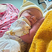 Adeline is registered to the contest to win money with this photo: newborn, baby, infant, sleeping, portrait, face, beanie, blanket, yellow_blanket, onesie, clothing, adult, caregiver, holding, cuddling, indoor, bedroom, cozy, cherry_pattern, peaceful